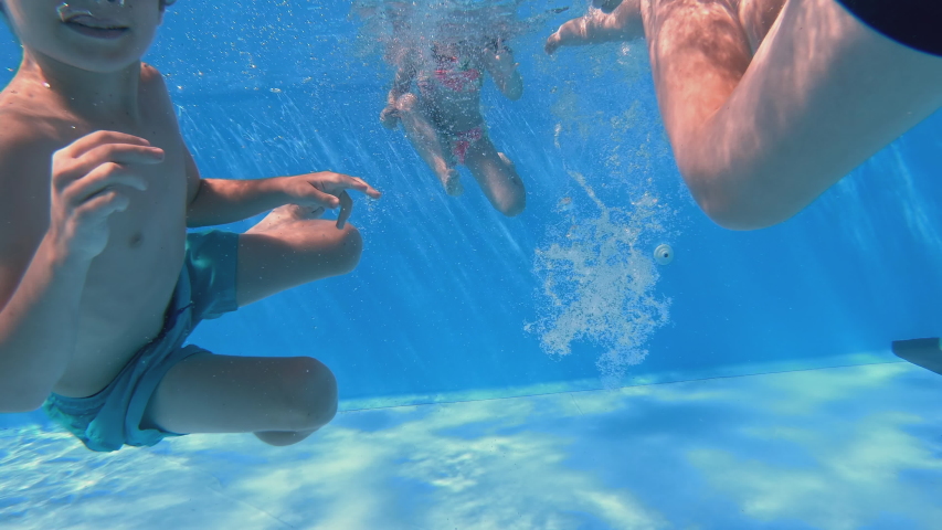 Children enjoying summer vacation. Underwater view of happy fun loving boy diving into swimming pool at a pool party in summer sunny day. Slow motion. | Shutterstock HD Video #1056771002