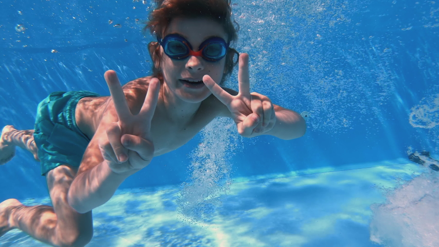 Children enjoying summer vacation. Underwater view of happy fun loving boy diving into swimming pool at a pool party in summer sunny day. Slow motion.
