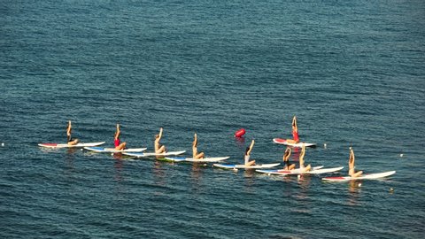 Group of young womens in swimsuit doing yoga on sup board in calm sea, early morning. Balanced pose - concept of healthy life and natural balance between body and mental development.