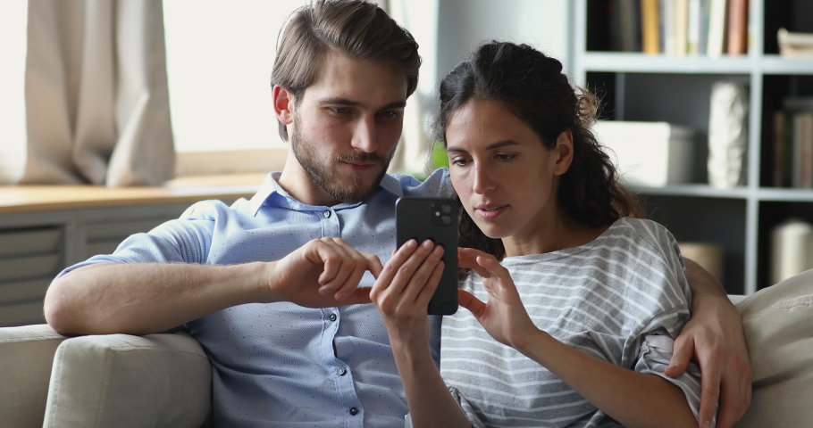 Surprised young family couple looking at mobile screen, feeling excited about online lottery win message. Overjoyed spouses winning giveaway in social networks, celebrating success together at home. | Shutterstock HD Video #1056771818