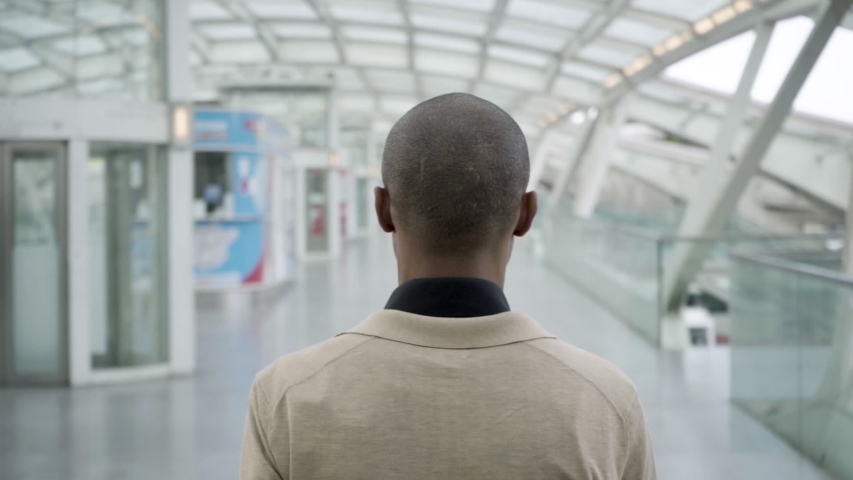 Back view of young black man in casual walking at train station. Closeup shot, slow motion. Passenger in terminal concept
