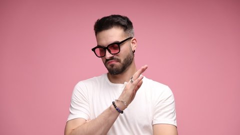 young casual man standing against pink background with his arms crossed, wearing sunglasses, shrugging his shoulders and gesturing that he has no idea about what someone is talking about