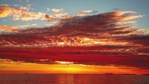 Time-lapse of the sun setting over the horizon at a romantic beach at the Croatian Mediterranean seaside with ships passing by. The water is moving gently while the clouds are turning red.