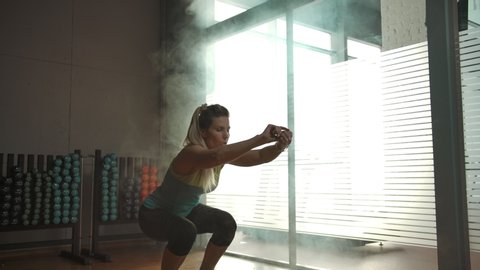 Caucasian woman is squatting on the hemisphere in the gym. Hard exercise for the buttocks. Smoke-filled gym, large windows, silhouette of a beautiful female body.