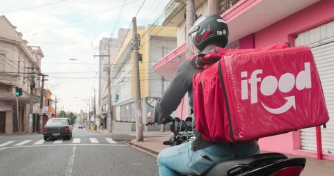 Ribeirão Preto, São Paulo  Brazil - Circa July 2020: Worker iFood on the motorcycle delivers food to customers in city. Editorial 4K.