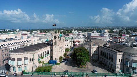 Drone moves over the roofs of houses from Barbados Parliament building with barbadian flag in Bridgetown