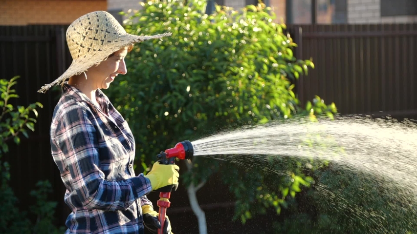 Young woman watering plants in her garden with garden hose. Hobby concept