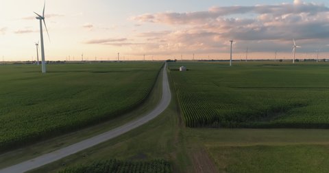 Flying backwards above countryside road and wind turbines standing on green field
