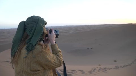 Slow motion of young Caucasian woman photographing sand dunes in desert, Morocco. High quality 4k footage