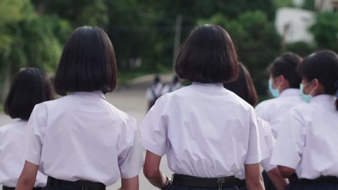 Slow motion of back view of Asian high school students in white uniforms on the semester start wearing masks and walking in the morning during the Coronavirus 2019 (Covid-19) epidemic.
