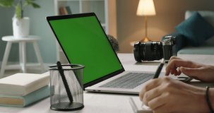 Close up shot of hands of student working with chroma key green screen laptop, using trackpad and pen with notebook in living room - technology concept 4k video template