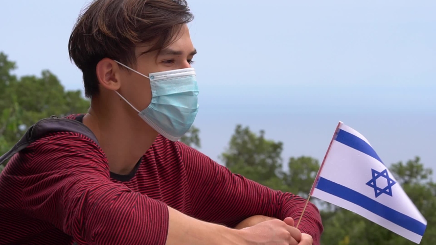Travel, vacation and summer holiday during the coronavirus outbreak. Tourism in the Israel and COVID-19 measures. A young man in a protective medical mask with the flag. Social distance Royalty-Free Stock Footage #1056804863