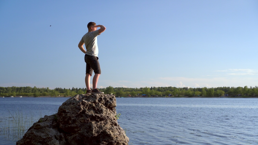 A young man stands on a stone near the river admiring the landscape. A man in nature.