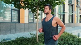 Young man exercising outside. Guy jogging on street alone and running forward among urban city. Strong powerful handsome man on video.