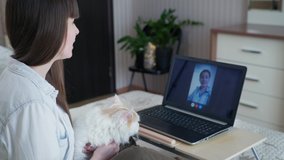 veterinary consultation, a lovely girl with her beloved cat communicates with a veterinarian using modern technology a webcam on a laptop