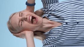 Scared desperate woman screaming and covering ears on blue background. She is annoyed with loud noise. Video with Vertical Screen Orientation 9:16