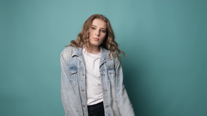 Happy girl with curly hair dancing and having fun over turquoise background. Positive mood.
