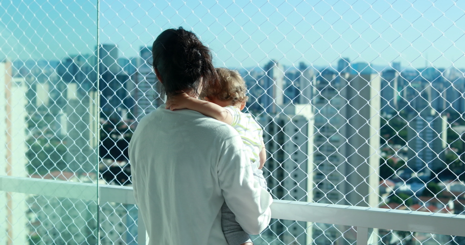 Mom holding baby looking at city view from apartment balcony with safety net
