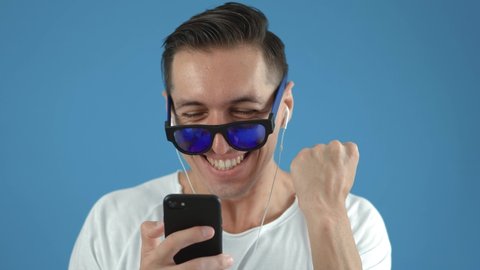 Surprised man winner hold smartphone read good news amazed by mobile online bet bid game win, happy male look at cell phone screen takes off sunglasses overjoyed by victory success