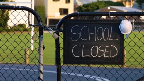 School closed sign with protective face mask hanging on a padlocked gate, school closed or shutdown concept amid coronavirus fears and panic over contagious virus