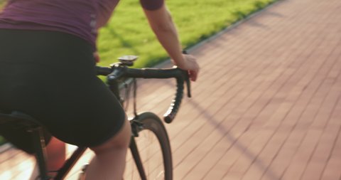 Fit woman cyclist cycles along bike trail. Woman is cycling. Female hands hold aero bike handlebar. Professional cycling athlete is pedaling on cycle path at sunset. Triathlon concept