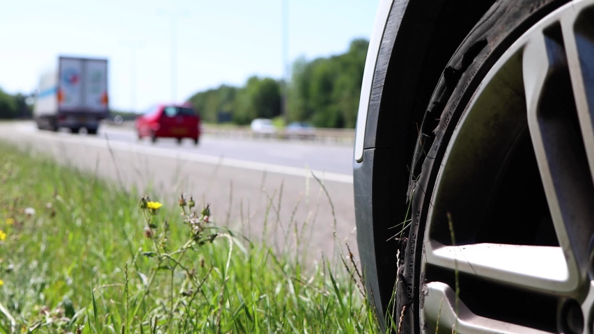 A car with a flat tyre after a large blow out on the highway showing a large slit in the tyre at the side of the M25 motorway in London in the UK Royalty-Free Stock Footage #1056837935
