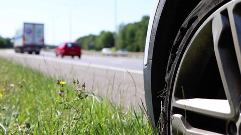 A car with a flat tyre after a large blow out on the highway showing a large slit in the tyre at the side of the M25 motorway in London in the UK