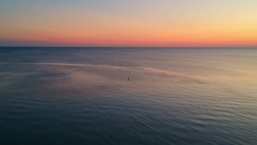 Aerial lake view going backwards revealing a beach path nature trail at sunrise.
