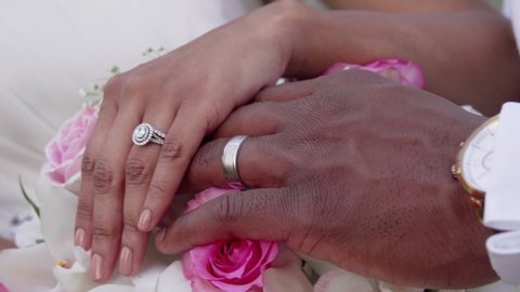 African American couple display wedding rings on top of a floral bouquet on their wedding day. Close up handheld in Maui Hawaii. 