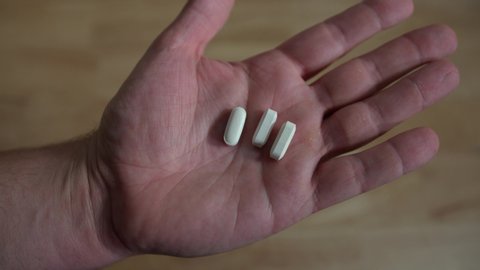 Closeup of hand opening to reveal holding a couple of generic white pills