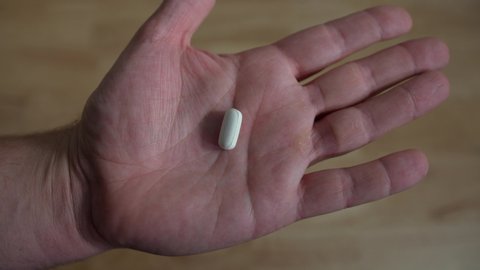 Hand opening up to reveal single white pill in man's hand, closeup 4k