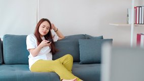 Asian young woman sitting on couch watching movie on TV in living room at home.