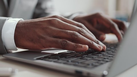 Close up view of hands of unrecognizable African American businessman in formalwear typing on laptop while working at desk in office