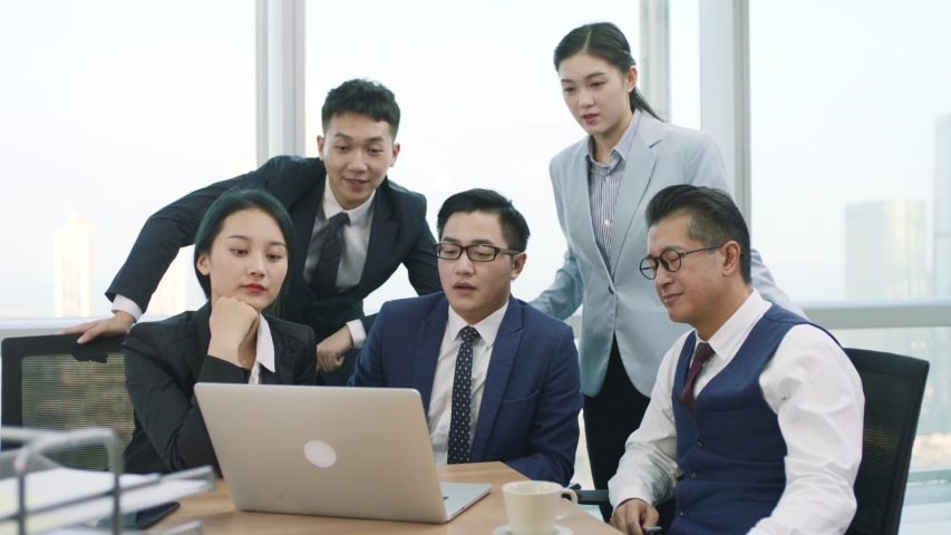Team of five asian corporate executives meeting in office discussing business using laptop computer in modern corporation