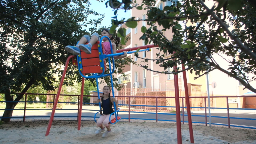 Two little pretty sisters, five and eight years old, having fun at the playground made in marine theme. Children swinging on swings on sunny summer day . 50 fps slow motion Royalty-Free Stock Footage #1056847556