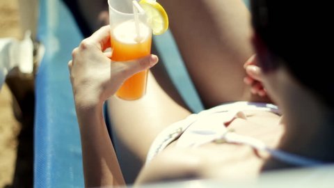 Woman in bikini lying on sunbed and drinking cocktail, top view
