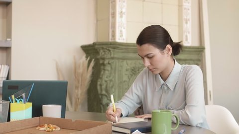 Medium shot of young Asian man wearing shirt of pastel color is sitting at desk and writing essay