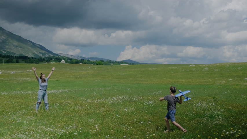 Mother with her son play together with a toy blue plane on a meadow with flowers against a background of mountains in Montenegro. 
