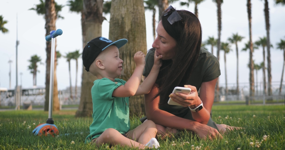 Young mother and little son on the grass in a tropical park among palm trees. Happy family concept.