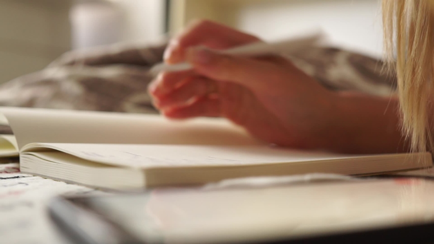 Girl makes notes in a notebook. Hand writes. Girl doing her homework. Remote study. Woman makes plans for the future, doing academic research preparing for exam coursework studying at home on a bed Royalty-Free Stock Footage #1056859841