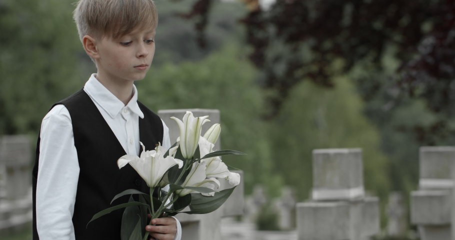 Close up view of boy teenager putting white lily flowers on gravestone of his father. Young kid honoring his dad soldier at cemetery. Concept of memorial day. Royalty-Free Stock Footage #1056860630