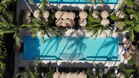 Drone flying through Miami beach beautiful three swimming pools filled with palm trees in the middle of summer vacation. Florida weather is amazing location for fun seekers