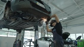 Car service worker welds and repairs an exhaust pipe of a car. Close-up welding work on a lifted car. View from the back. Mechanic welds the bottom of the car. - Powered by Shutterstock - Get 15% off with code: PIKWIZARD15