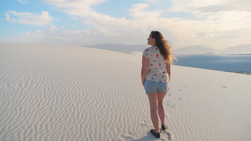 Young girl walking on white sand dunes in New Mexico desert national monument hill during sunset back point of view behind following