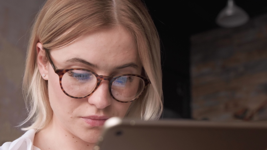 Close Up Young Blonde woman in fashion glasses eye looking monitor, surfing Internet. Stylish Blonde working with laptop or Tablet from home in her home office. The Monitor Screen Is Reflected In The  Royalty-Free Stock Footage #1056867389
