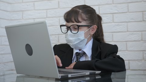 Stay at home business. A little girl like a boss in medical mask work on notebook. A happy child takes off her protective mask, a concept of the end of coronavirus pandemic.