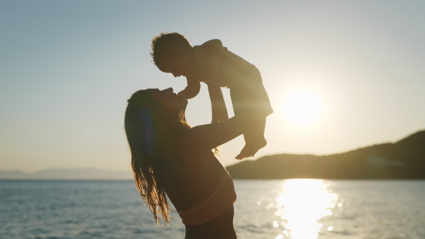 Authentic close up shot of an young neo mother is keeping on her arms and playing with a newborn baby on a seaside beach at sunset during holiday vacation. | Shutterstock HD Video #1056868742