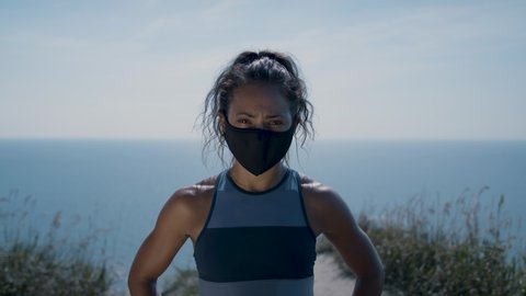 Top of the world. Portrait of an athletic woman on a cliff's edge in a mask. Working out with a mask on. Pandemic exercising. Shot in 4k.  