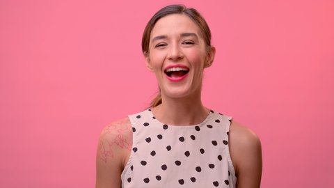 Young woman looking at the camera smiling and winking on pink background. Woman in summer dress posing in front of the camera in a photo studio.