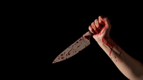 Human hand with bloodstained knife shot on black background. Woman's hand in blood holds knife and strike. Concept of violence, murder with kitchen knife
